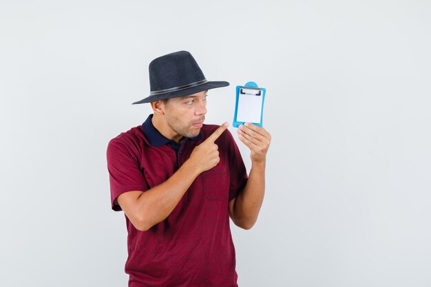 Jeune homme pointant sur le presse-papiers en t-shirt, vue de face de chapeau.