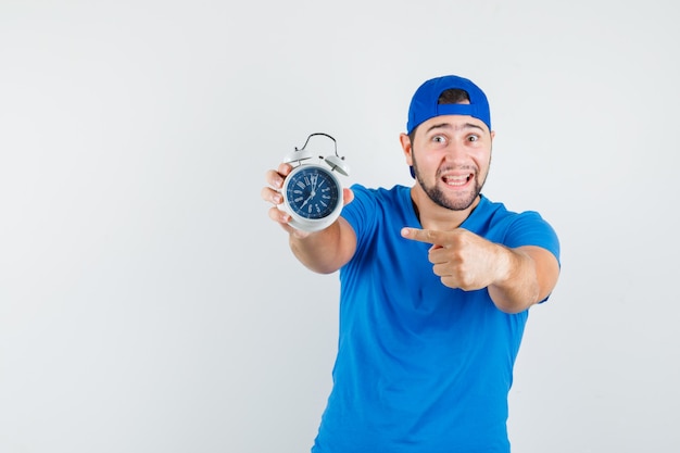 Jeune homme pointant sur réveil en t-shirt bleu et casquette et à la recherche positive