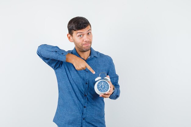 Jeune homme pointant sur réveil en vue de face de chemise bleue.