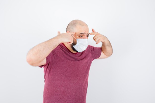 Jeune homme pointant sur ses tempes en t-shirt rose, vue de face du masque.