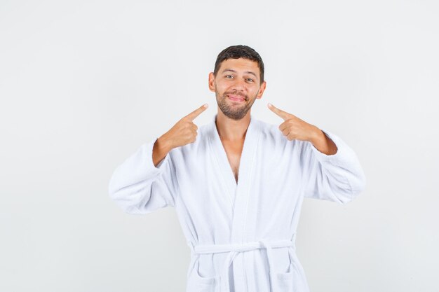 Jeune homme pointant sur son sourire en vue de face de peignoir blanc.