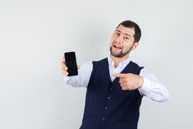 Jeune homme pointant sur téléphone mobile en chemise, gilet et à la satisfaction