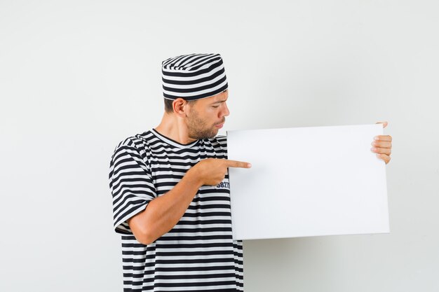 Jeune homme pointant sur une toile vierge en chapeau t-shirt rayé et à la recherche concentrée