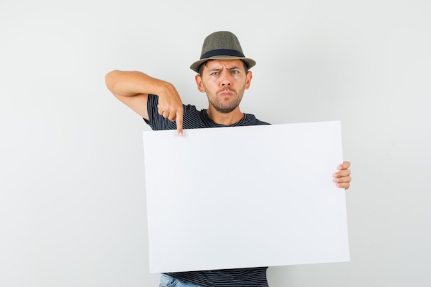 Jeune homme pointant sur toile vierge en t-shirt jeans hat et à la sérieuse