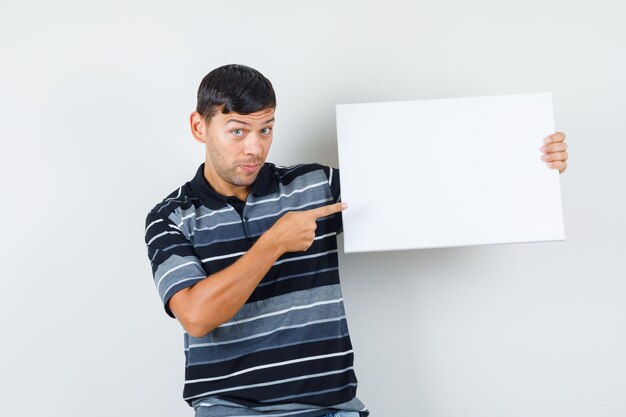 Jeune homme pointant sur une toile vierge en t-shirt, vue de face.