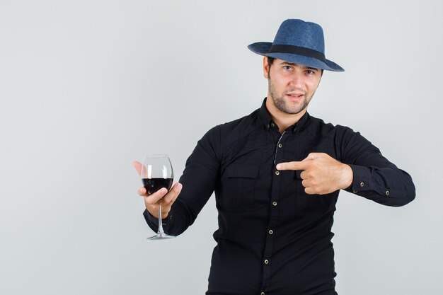 Jeune homme pointant sur un verre d'alcool en chemise noire