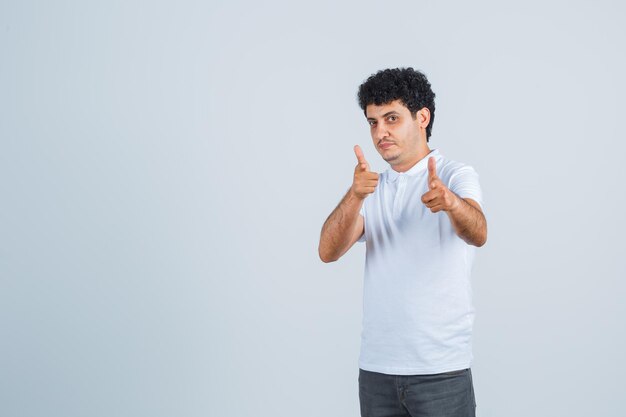 Jeune homme pointant vers la caméra avec l'index en t-shirt blanc et jeans et regardant sérieux, vue de face.