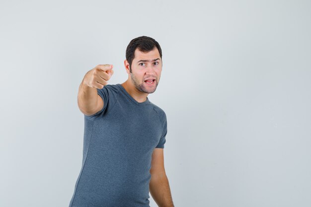 Jeune homme pointant vers la caméra en t-shirt gris et à la confiance