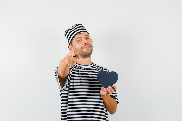 Jeune homme pointant vers la caméra tenant présent fort en chapeau t-shirt rayé et à la joyeuse