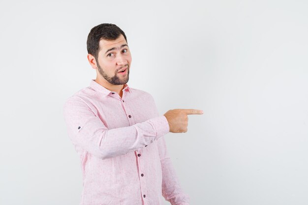 Jeune homme pointant vers le côté en chemise rose et à la recherche positive