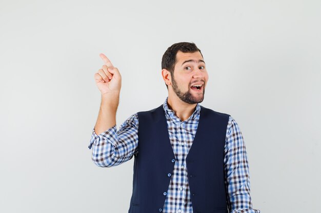 Jeune homme pointant vers le côté avec le doigt en chemise, gilet et à la joyeuse