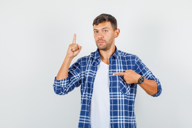 Jeune homme pointant vers le côté avec le doigt en chemise et à la vue de face stricte.