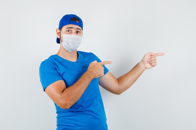 Jeune homme pointant vers le côté en t-shirt bleu et casquette, masque