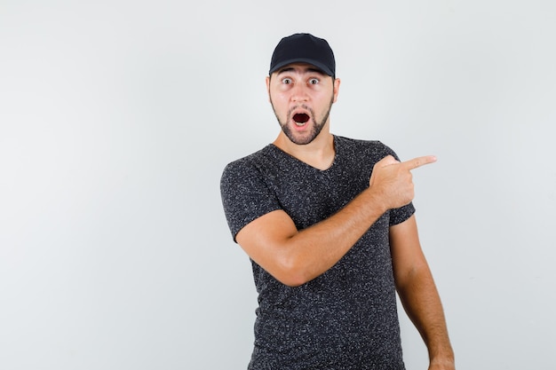 Jeune homme pointant vers le côté en t-shirt et casquette et à la surprise