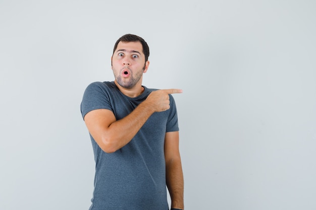 Jeune Homme Pointant Vers Le Côté En T-shirt Gris Et à La Surprise