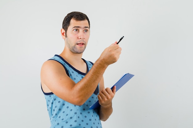 Jeune homme pointant vers l'extérieur, tenant le presse-papiers en maillot bleu et à la perplexité. vue de face.