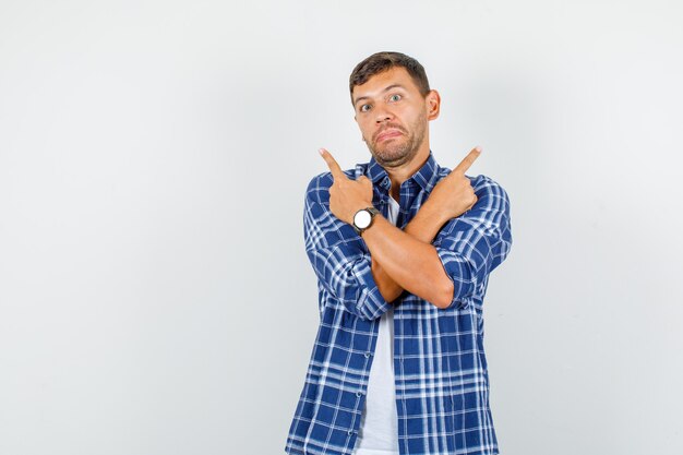 Jeune homme pointant vers le haut avec les bras croisés en chemise et à la confusion. vue de face.