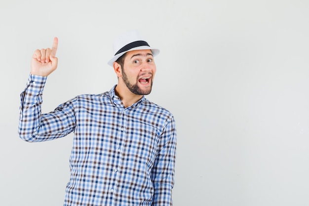 Jeune homme pointant vers le haut en chemise à carreaux, chapeau et à la gaieté.