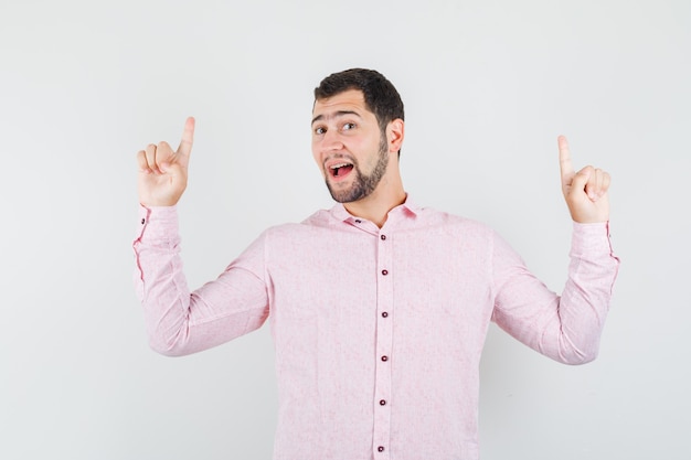 Jeune homme pointant vers le haut en chemise rose et à la joyeuse