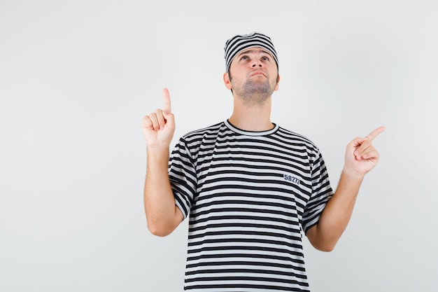 Jeune homme pointant vers le haut et de côté en t-shirt, chapeau et à la recherche d'espoir. vue de face.