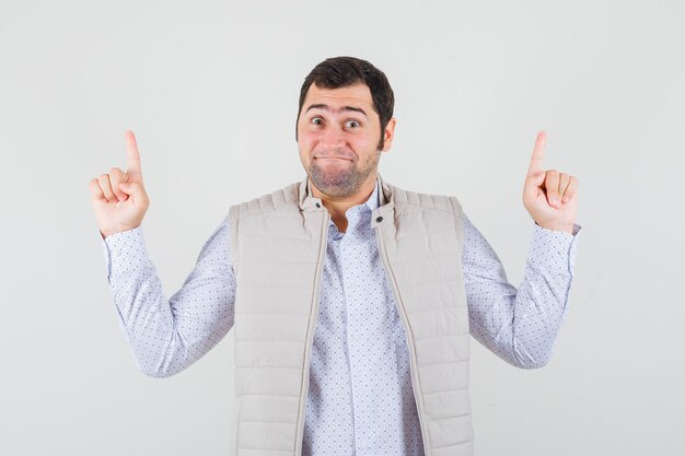 Jeune homme pointant vers le haut avec l'index en veste beige et à la recherche d'optimiste. vue de face.