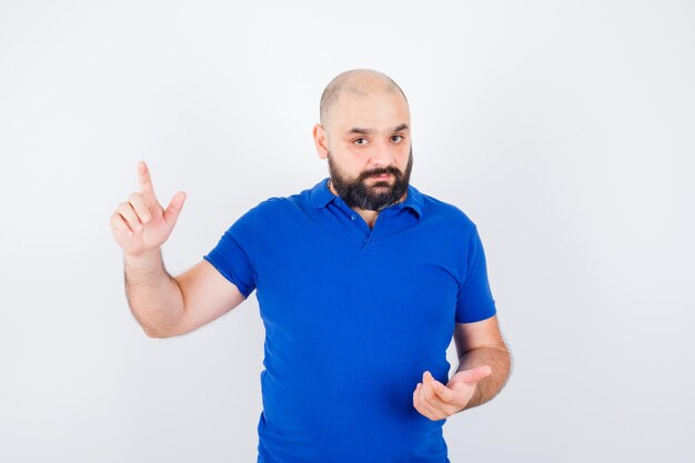 Jeune homme pointant vers le haut en pensant en chemise bleue et en regardant concentré. vue de face.