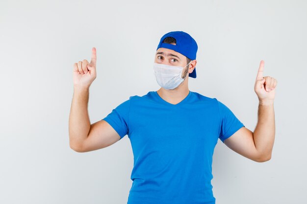 Jeune homme pointant vers le haut en t-shirt bleu et casquette, masque et à la confiance