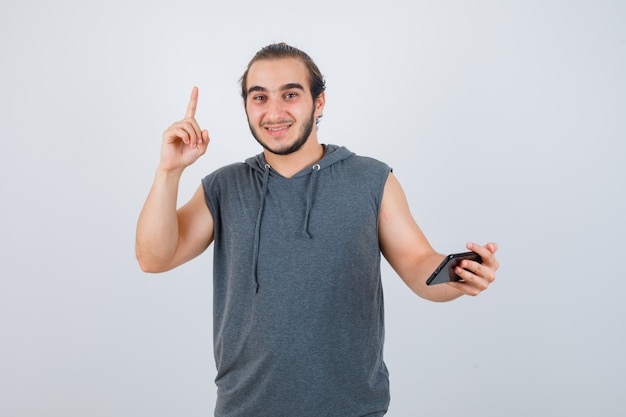 Jeune homme pointant vers le haut en t-shirt à capuche et à la vue de face, heureux.