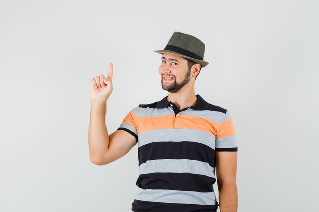 Jeune homme pointant vers le haut en t-shirt, chapeau et à la joyeuse