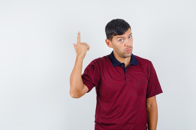 Jeune homme pointant vers le haut en t-shirt et hésitant, vue de face.