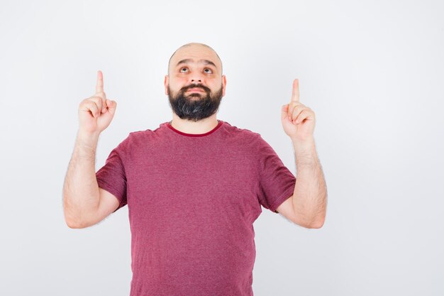 Jeune Homme Pointant Vers Le Haut En T-shirt Et Se Demandant. Vue De Face.