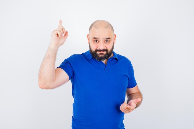 Jeune homme pointant vers le haut tout en regardant la caméra en chemise bleue et en regardant concentré. vue de face.