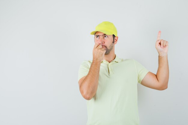 Jeune homme pointant vers le haut en uniforme jaune et regardant hésitant.