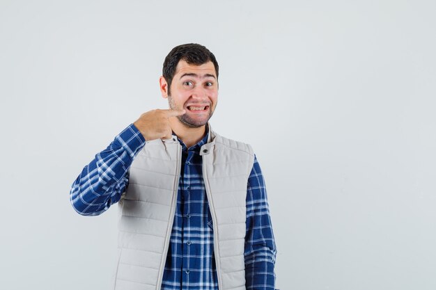 Jeune homme pointant vers ses dents en chemise, vue de face de la veste sans manches.