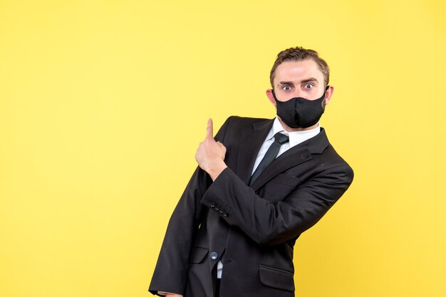 Photo gratuite jeune homme pointe un doigt en arrière sur jaune