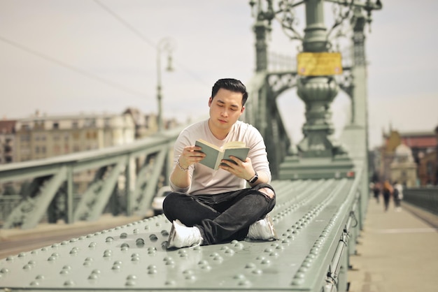 jeune homme sur un pont lit un livre