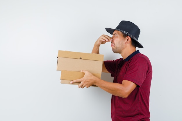 Jeune homme portant des boîtes en chemise rouge, chapeau noir et à la dégoût.