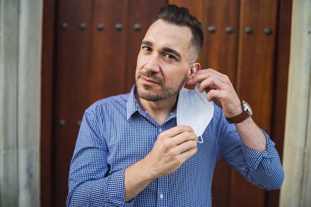 Jeune homme portant une chemise bleue debout à la porte avec un masque médical - concept Covid-19