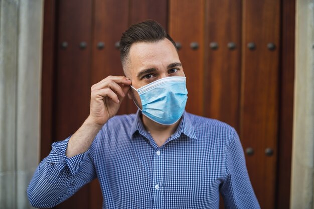 Jeune homme portant une chemise bleue debout à la porte avec un masque médical - concept Covid-19