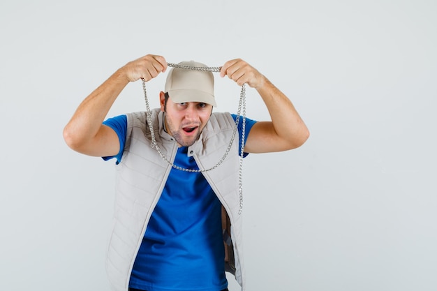 Photo gratuite jeune homme portant un collier chaîne en t-shirt, veste, casquette et à la vue excitée, avant