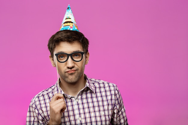 Jeune homme portant de fausses lunettes sur mur violet. Fête d'anniversaire.