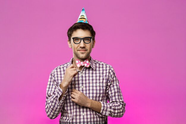 Jeune homme portant de fausses lunettes et papillon sur mur violet.