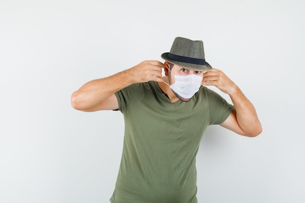 Jeune homme portant un masque médical en t-shirt vert et chapeau et à la recherche de sérieux