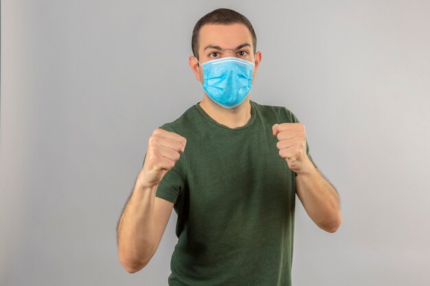 Jeune homme portant un masque médical avec visage en colère debout avec des poings de boxe, et prêt à attaquer isolé sur blanc