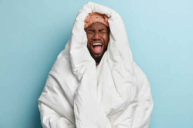 Jeune homme portant un masque de sommeil et enveloppé dans une couverture blanche