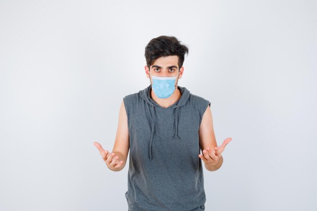 Jeune homme portant un masque tout en étirant les mains comme tenant quelque chose en t-shirt gris et ayant l'air sérieux