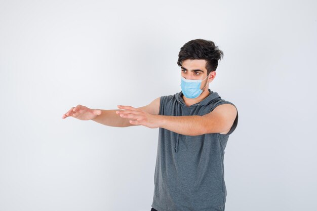 Jeune homme portant un masque tout en étirant les mains vers la gauche en t-shirt gris et l'air sérieux