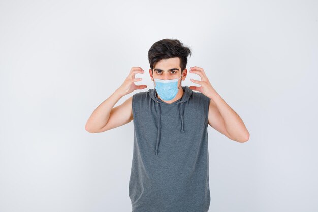 Jeune homme portant un masque tout en se tenant la main près du visage en t-shirt gris et l'air sérieux