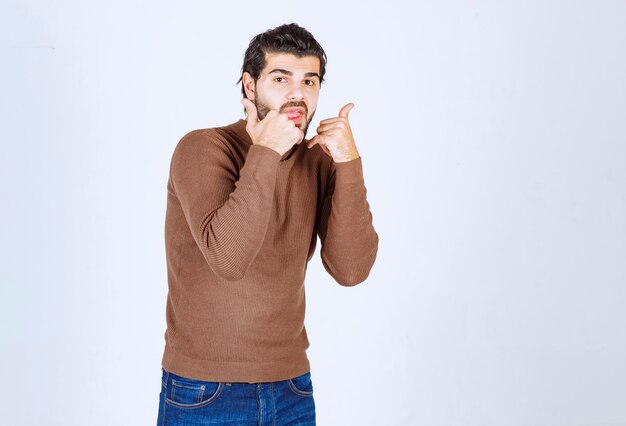 Jeune homme portant un pull décontracté debout sur un fond blanc isolé faisant le geste de parler au téléphone. photo de haute qualité