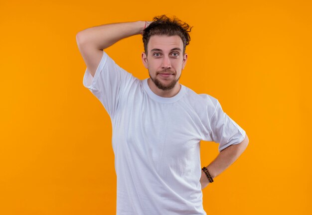 Jeune homme portant un t-shirt blanc a mis sa main sur la tête sur un mur orange isolé